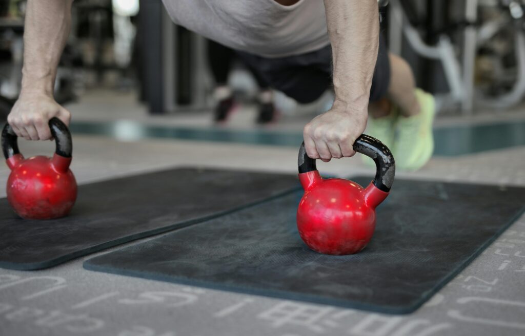 Close-up of a man doing plank push-ups using kettlebells in a gym. Focus on fitness and strength.