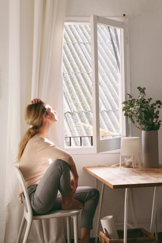 A serene moment as a woman enjoys sunshine near a window in a cozy interior setting.