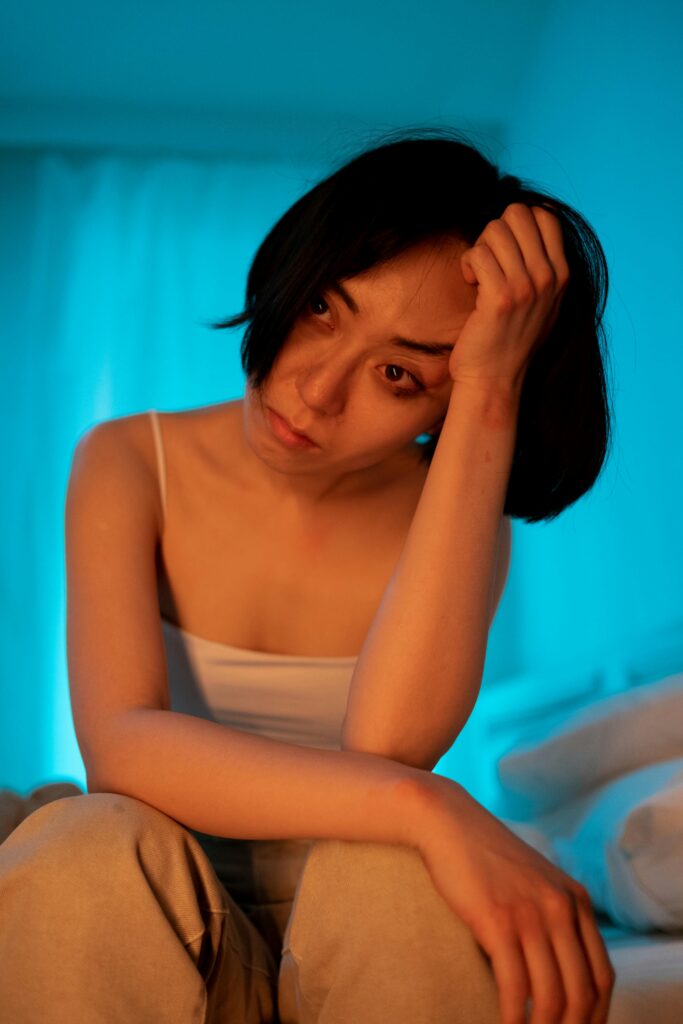 Thoughtful woman sits in soft blue light, capturing a moment of introspection and emotion.