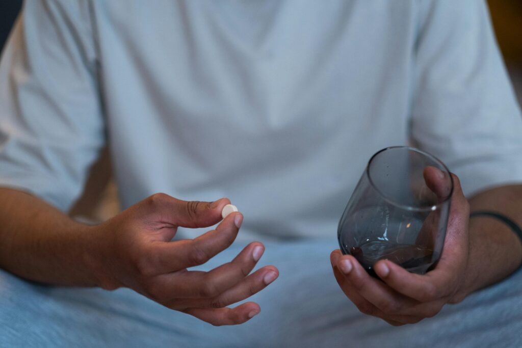 Close-up of an unrecognizable man taking a pill with a glass. Indoor setting.